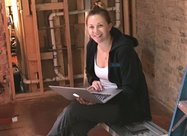 Sally Anderson Little working on a laptop at a gutted job site